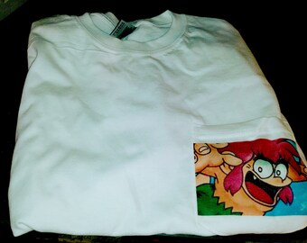 Könnte beinhalten: Weißes T-Shirt mit einer Tasche, die einen Comic-Charakter mit roten Haaren und einem grünen Shirt zeigt. Der Charakter lächelt und hat einen großen Mund.