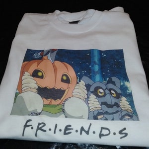 May include: White t-shirt with a printed image of two cartoon characters. The characters are a pumpkin with a toothy grin and a gray creature with large eyes. The text "F.R.I.E.N.D.S" is printed below the image.