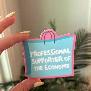 May include: A sticker in the shape of a shopping bag with the text "PROFESSIONAL SUPPORTER OF THE ECONOMY" in white on a light blue background. The bag has a pink border and pink handles.