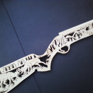 May include: A wooden cutout of a rifle with a forest scene and deer carved into the wood.