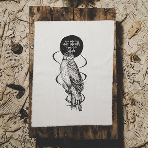 Peut inclure: Une illustration en noir et blanc d'un hibou avec le texte "We possess a power far greater than the visible" imprimé au-dessus. L'illustration est encadrée dans un cadre en bois et affichée sur une nappe en dentelle blanche.