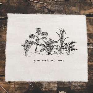 May include: A white canvas tote bag with a black line drawing of a garden with the text "grow food, not lawns".