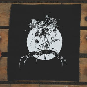 Peut inclure: Patch en tissu noir avec un motif blanc d'un bouquet de fleurs et d'une pleine lune. Le texte "It's not got to fade to let go" est écrit sur une bannière sous la lune.