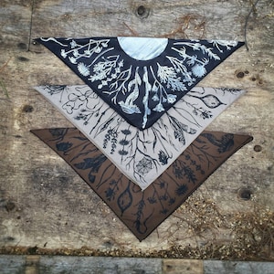 May include: Three triangular fabric bandanas with a black and white botanical print. The top bandana features a moon and stars design. The middle bandana is a light beige colour. The bottom bandana is a dark brown colour.