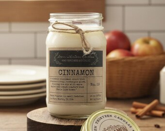 May include: A glass jar candle with a cinnamon scent, labeled "Cinnamon" with a description of the scent. The candle sits on a small wooden stand, with a lid nearby. The label reads "Loem Thirteen Candles".
