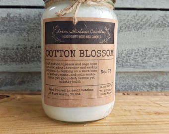 May include: A glass jar candle with a gold lid and a twine bow. The label reads Cotton Blossom, Loem Thirteen Candles, Hand Poured Wood Wick Candles, No. 73, 14 oz (397 g), 75-80 hour burn time, and details about the scent profile and origin.