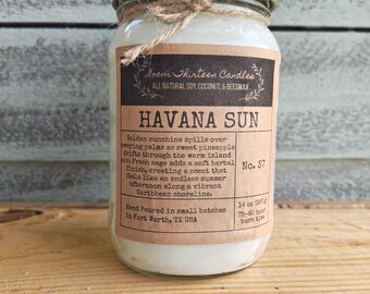 May include: A 14 oz candle in a clear glass jar with a gold metal lid and a tied jute twine bow. The label reads Loem Thirteen Candles, Havana Sun, No. 37, and describes the scent notes of pineapple and sage, noting 75-80 hours of burn time.