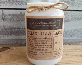May include: A white candle in a clear glass jar with a brown paper label featuring the text Chantilly Lace, No. 36, and Loem Thirteen Candles. The label lists ingredients and a 14 oz weight. A jute twine bow is tied around the jar neck.