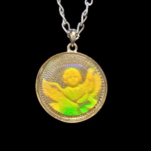 May include: A silver chain necklace with a round pendant featuring an iridescent image of an angel with wings. The angel is surrounded by a green and yellow halo.