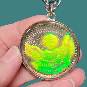 May include: A silver chain necklace with a round pendant featuring a green and yellow sun and mountain scene.
