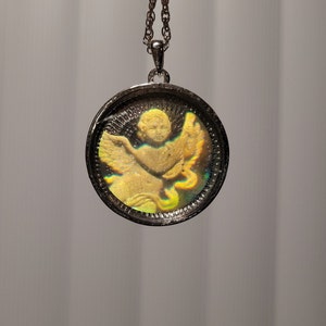 May include: A silver chain necklace with a round pendant featuring a gold-toned cherub with iridescent wings.