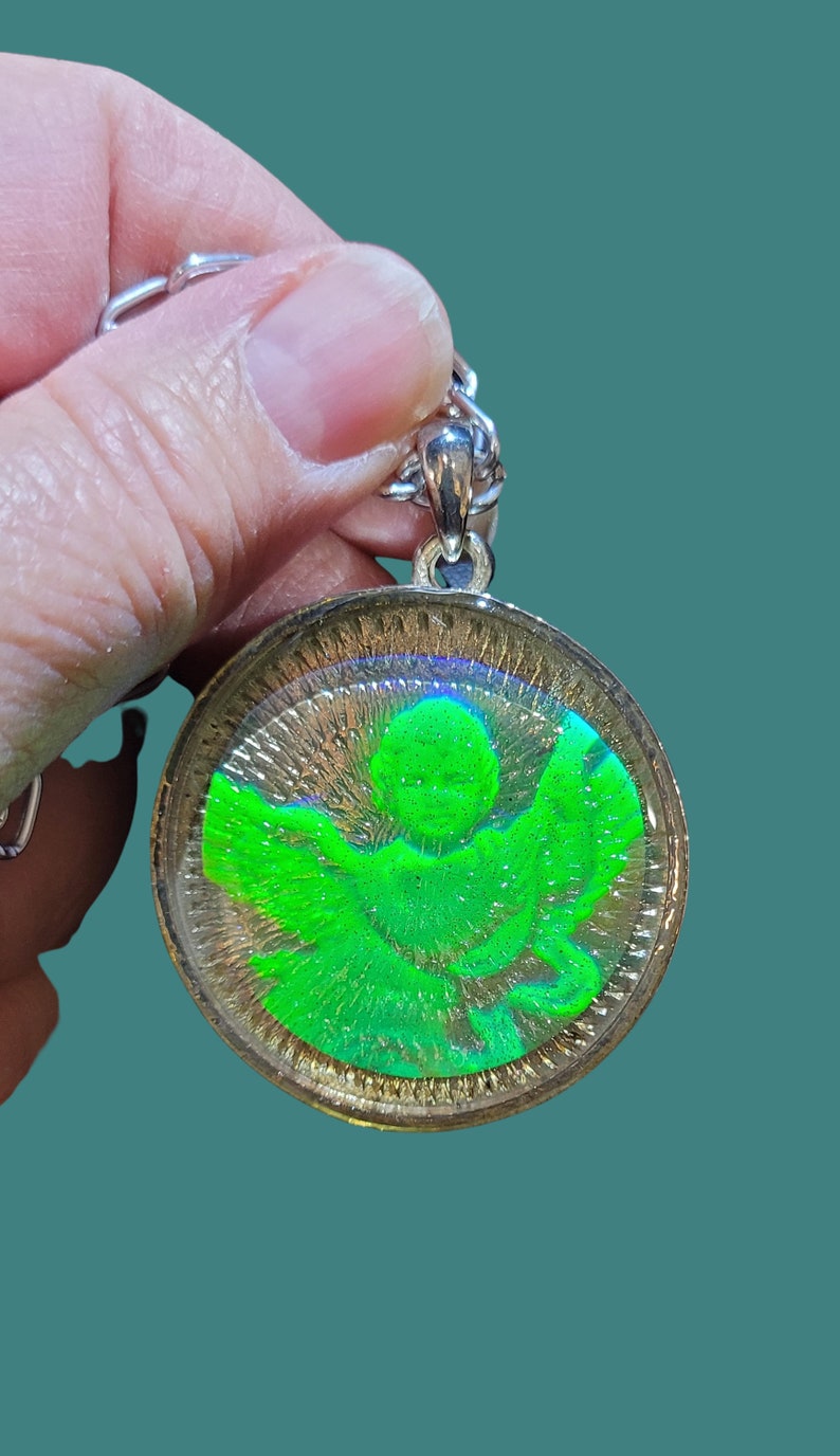 May include: A silver chain with a round pendant featuring a green angel with iridescent wings inside a clear resin dome.