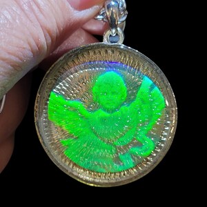 May include: A silver chain necklace with a round pendant featuring a green angel with iridescent wings. The pendant is encased in clear resin.