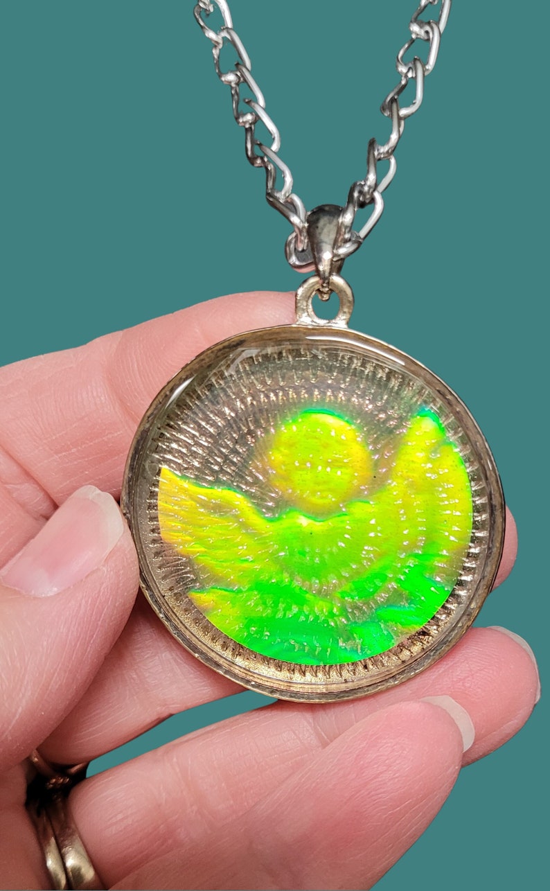 May include: A silver chain necklace with a round pendant featuring a green and yellow sun and mountain scene.