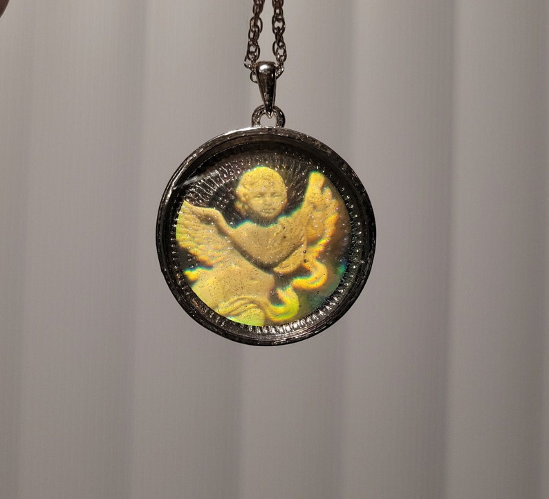 May include: A silver chain necklace with a round pendant featuring a gold-toned cherub with iridescent wings.