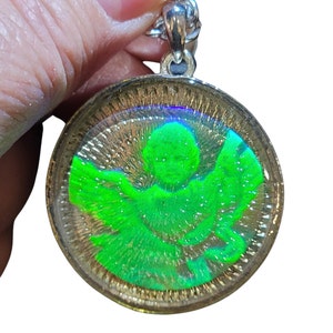 May include: A silver chain necklace with a round pendant featuring a green angel with wings inside a clear resin dome.