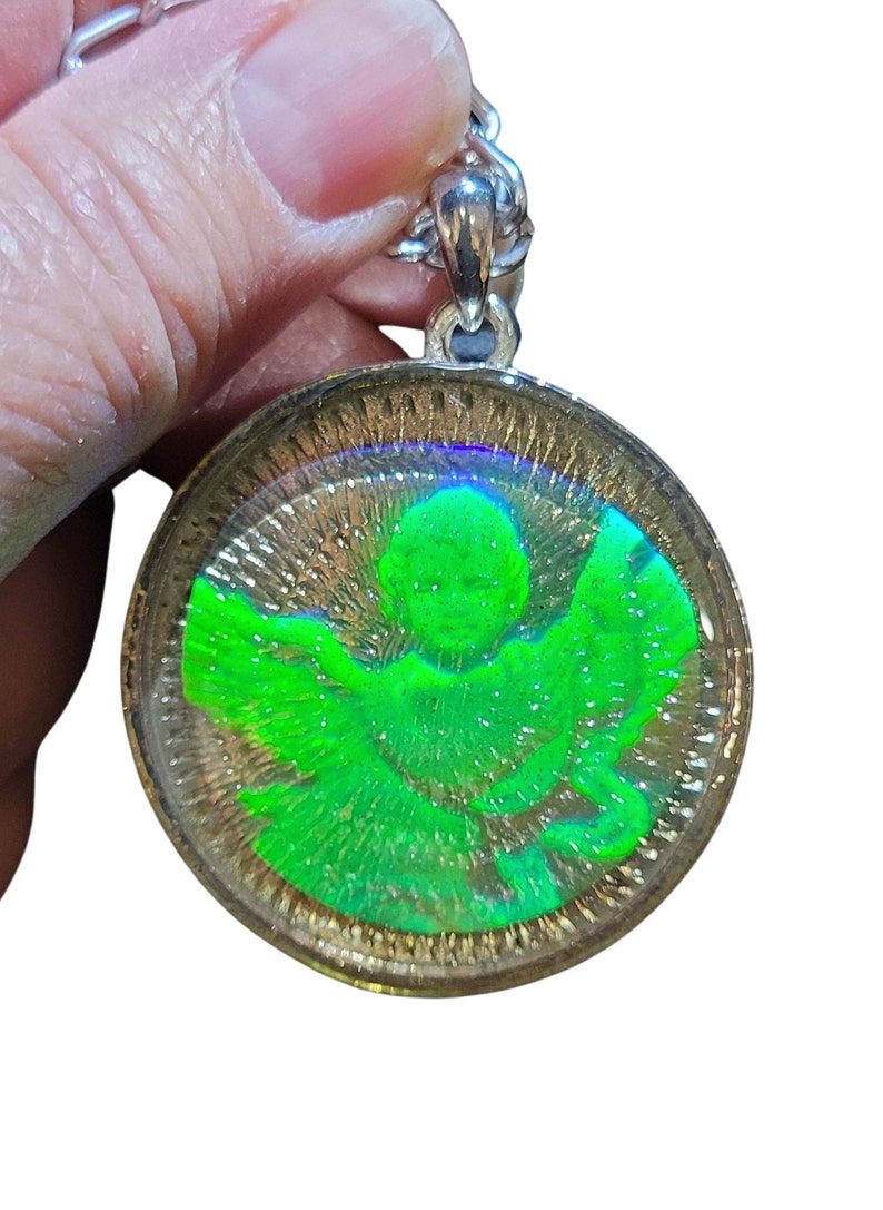 May include: A silver chain necklace with a round pendant featuring a green angel with wings inside a clear resin dome.