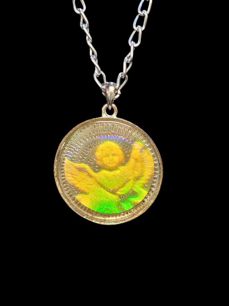 May include: A silver chain necklace with a round pendant featuring an iridescent image of an angel with wings. The angel is surrounded by a green and yellow halo.
