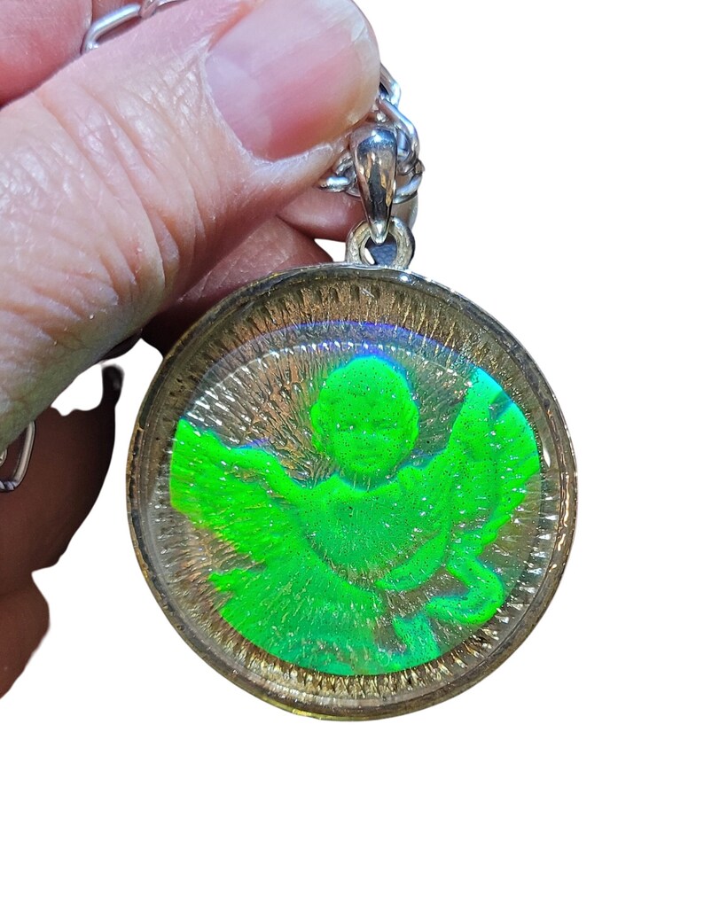 May include: A silver chain with a round pendant featuring a green angel inside a clear resin dome.