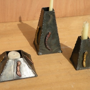 May include: Three metal candle holders with a geometric design. Each holder has a different size and features decorative metal accents.