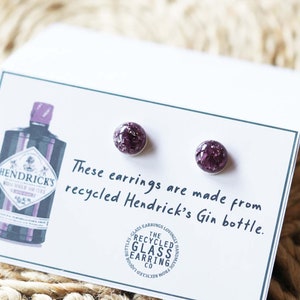 Może przedstawiać: Para fioletowych szklanych kolczyków wykonanych z recyklingowanej butelki ginu Hendricks. Kolczyki znajdują się na białej kartce z tekstem "These earrings are made from recycled Hendricks' Gin bottle."