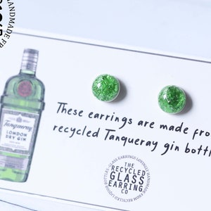 May include: A pair of green glass earrings made from recycled Tanqueray gin bottles. The earrings are on a white card with the text "These earrings are made from recycled Tanqueray gin bottle."