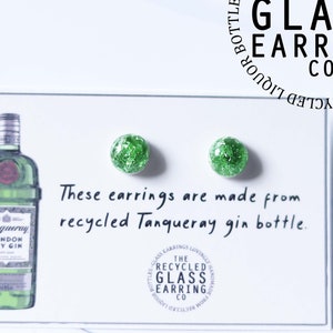 May include: A pair of green glass earrings made from recycled Tanqueray gin bottles. The earrings are displayed on a white card with the text "These earrings are made from recycled Tanqueray gin bottle." and a logo for "The Recycled Glass Earring Co."