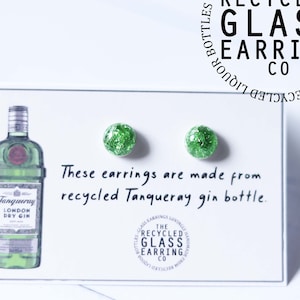 Op de afbeelding: Een paar groene glazen oorbellen gemaakt van gerecyclede Tanqueray-ginflessen. De oorbellen worden getoond op een witte kaart met de tekst "Deze oorbellen zijn gemaakt van gerecyclede Tanqueray-ginflessen." en een logo voor "The Recycled Glass Earring Co."