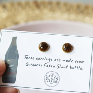 Peut inclure: Une paire de boucles d'oreilles en verre brun faites &agrave; partir d'une bouteille de Guinness Extra Stout recycl&eacute;e. Les boucles d'oreilles sont sur une carte blanche avec le texte "Ces boucles d'oreilles sont faites &agrave; partir d'une bouteille de Guinness Extra Stout." et un logo pour "The Recycled Glass Earring Co."