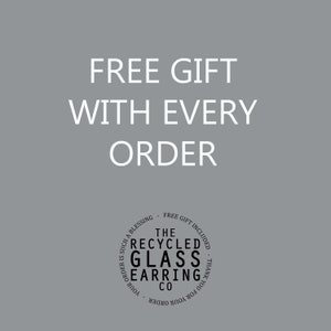 May include: A white text graphic on a gray background that reads "FREE GIFT WITH EVERY ORDER". Below the text is a black and white circle graphic that reads "THE RECYCLED GLASS EARRING CO. YOUR ORDER IS SUCH A BLESSING - FREE GIFT INCLUDED - THANK YOU FOR YOUR ORDER".