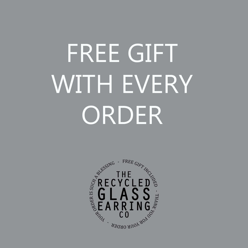 May include: A white text graphic on a gray background that reads "FREE GIFT WITH EVERY ORDER". Below the text is a black and white circle graphic that reads "THE RECYCLED GLASS EARRING CO. YOUR ORDER IS SUCH A BLESSING - FREE GIFT INCLUDED - THANK YOU FOR YOUR ORDER".
