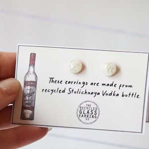 以下が含まれることがあります： リサイクルされたストリチナヤ・ウォッカのボトルから作られた、白いガラスのイヤリングのペア。イヤリングは、白いカードに「これらのイヤリングは、リサイクルされたストリチナヤ・ウォッカのボトルから作られています。」というテキストと、ストリチナヤ・ウォッカのボトルの絵が描かれています。
