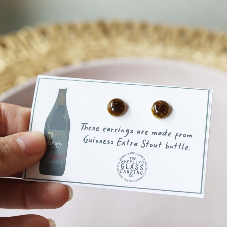 Peut inclure: Une paire de boucles d'oreilles en verre brun faites &agrave; partir d'une bouteille de Guinness Extra Stout recycl&eacute;e. Les boucles d'oreilles sont sur une carte blanche avec le texte "Ces boucles d'oreilles sont faites &agrave; partir d'une bouteille de Guinness Extra Stout." et un logo pour "The Recycled Glass Earring Co."