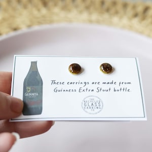 Peut inclure: Une paire de boucles d'oreilles en verre brun et or fabriqu&eacute;es &agrave; partir d'une bouteille de Guinness Extra Stout recycl&eacute;e. Les boucles d'oreilles sont pr&eacute;sent&eacute;es sur une carte blanche avec le texte "Ces boucles d'oreilles sont faites &agrave; partir d'une bouteille de Guinness Extra Stout." et un logo pour "The Recycled Glass Earring Co."