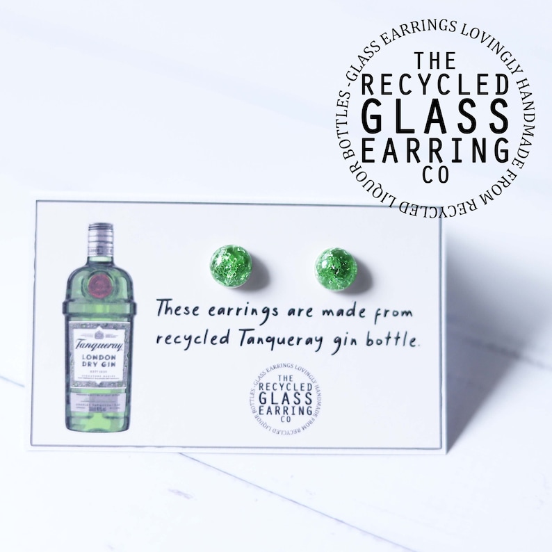 May include: A pair of green glass earrings made from recycled Tanqueray gin bottles. The earrings are displayed on a white card with the text "These earrings are made from recycled Tanqueray gin bottle." and a logo for "The Recycled Glass Earring Co."