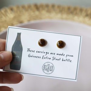 Peut inclure: Une paire de boucles d'oreilles en verre brun fabriqu&eacute;es &agrave; partir de bouteilles de Guinness Extra Stout recycl&eacute;es. Les boucles d'oreilles sont pr&eacute;sent&eacute;es sur une carte blanche avec le texte "Ces boucles d'oreilles sont faites &agrave; partir de bouteilles de Guinness Extra Stout." et un logo pour "The Recycled Glass Earring Co."