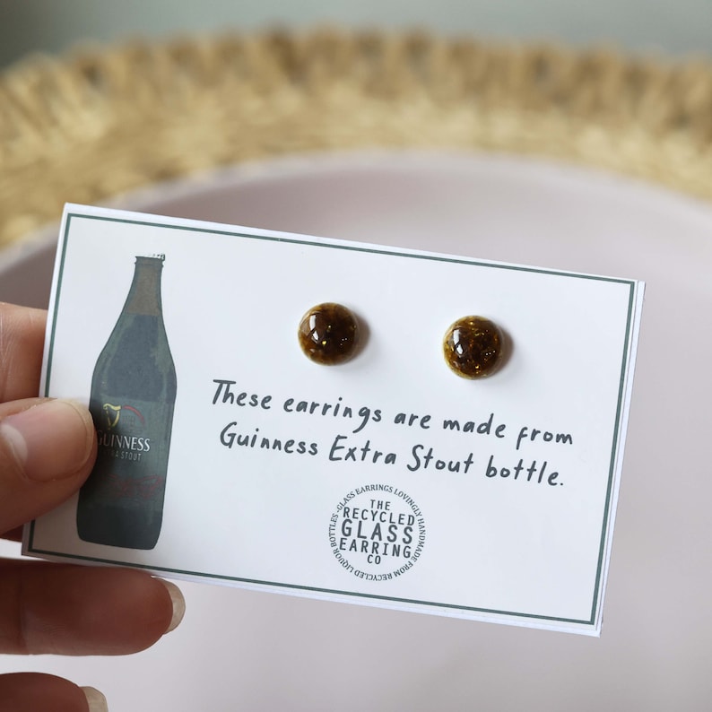 Peut inclure: Une paire de boucles d'oreilles en verre brun fabriqu&eacute;es &agrave; partir de bouteilles de Guinness Extra Stout recycl&eacute;es. Les boucles d'oreilles sont pr&eacute;sent&eacute;es sur une carte blanche avec le texte "Ces boucles d'oreilles sont faites &agrave; partir de bouteilles de Guinness Extra Stout." et un logo pour "The Recycled Glass Earring Co."