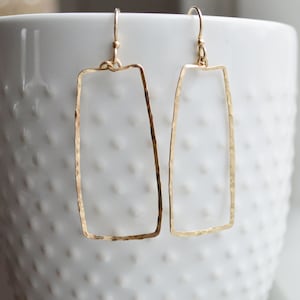May include: A pair of gold-toned rectangle shaped dangle earrings with a hammered texture.