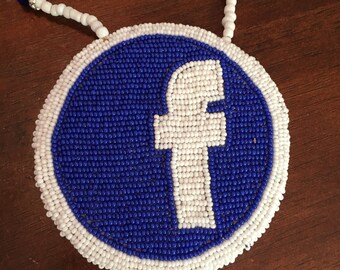 May include: A beaded necklace with a round pendant featuring the Facebook logo. The pendant is made of blue and white beads, and the logo is white on a blue background.