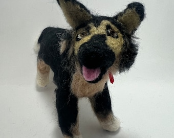 May include: A handmade felted German Shepherd dog figurine. The dog has black, tan, and white wool details. It has a red collar and a pink tongue. The dog is standing on a white surface.