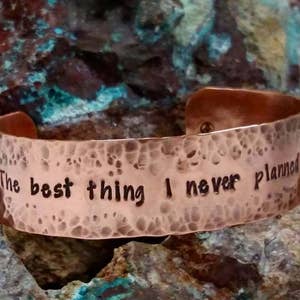 May include: A hammered copper bracelet with the inscription "The best thing I never planned".