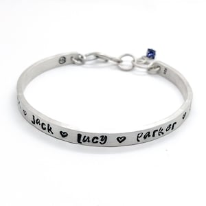 May include: Silver bangle bracelet with a personalized inscription that reads "Jack ♥ Lucy ♥ Parker".
