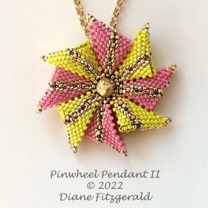 Pode incluir: Um pingente de cata-vento de contas rosa e amarelo com uma corrente dourada e uma conta dourada no centro. O pingente é etiquetado como "Pinwheel Pendant II © 2022 Diane Fitzgerald".