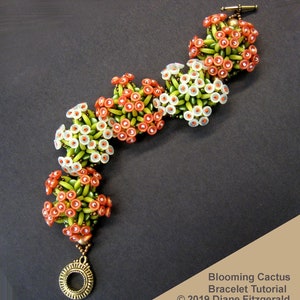 Puede incluir: Un brazalete de cuentas con un diseño de cactus en flor. El brazalete está hecho con cuentas verdes, blancas y naranjas. El brazalete tiene un cierre dorado y un pequeño dije dorado.