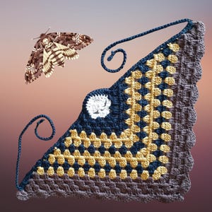 May include: A handmade crochet shawl in a triangular shape, featuring a color block design in navy blue, gold, and gray. A white skull-like motif is centered on the shawl. A Death's-head hawkmoth is positioned above the shawl.