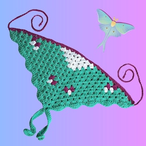 May include: A handmade crochet top in teal, white, and burgundy. The top features a scalloped edge and tie closures. A cartoon illustration of a luna moth is in the background.