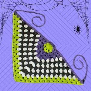 May include: A green, white, and gray crocheted triangle scarf with a purple skull design. The scarf has a long, thin tie that can be tied around the neck.