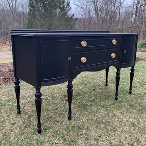 May include: A black painted antique sideboard with gold hardware and turned legs. The sideboard has two drawers and two doors.