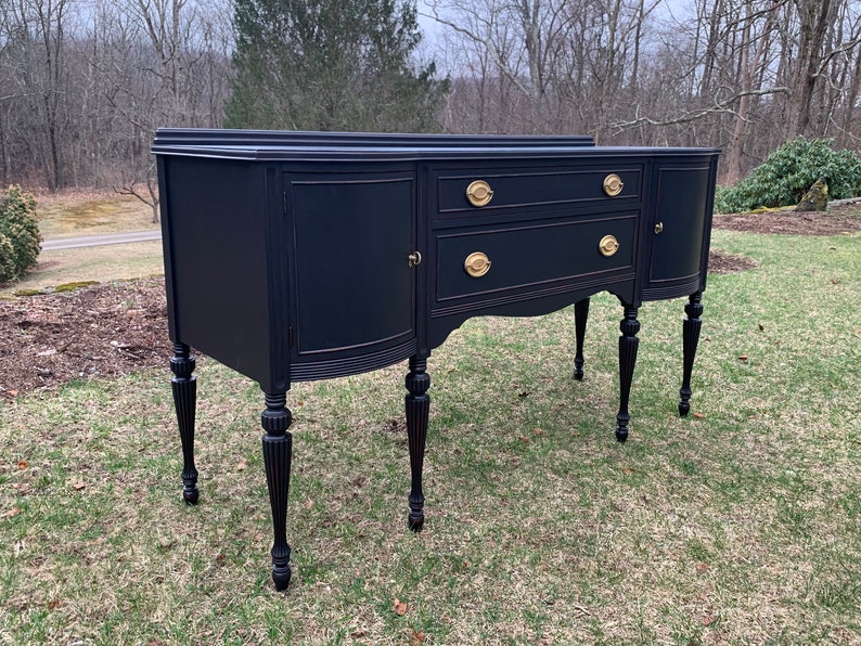 May include: A black painted antique sideboard with gold hardware and turned legs. The sideboard has two drawers and two doors.