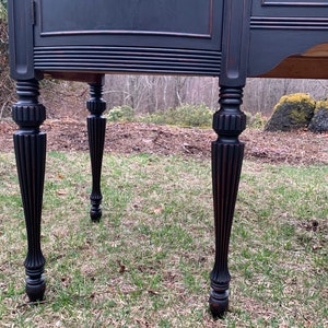 May include: Close-up of the black painted legs of a vintage buffet. The legs are turned and have a fluted design.